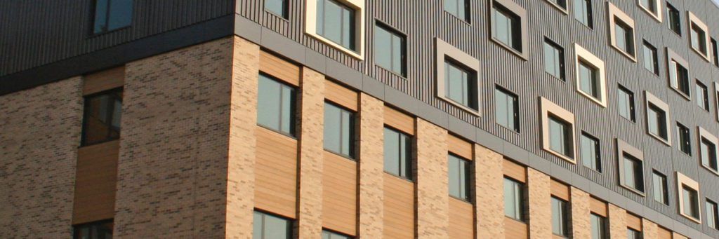 Close-up of a residential building's external wall build-up showing brick, insulated render and rainscreen cladding panels