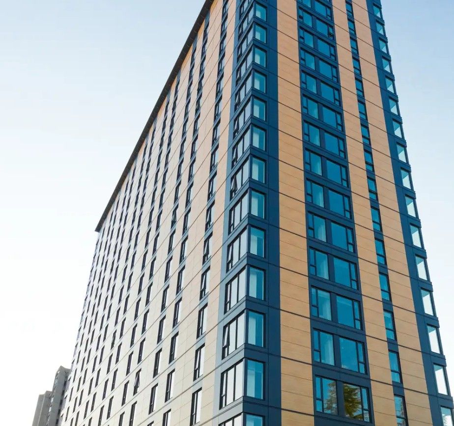 Tall high-rise residential tower with vertical cladding panels, viewed from street level