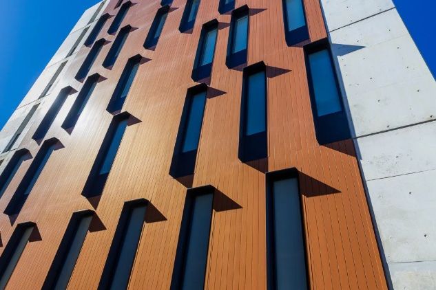 Upward view of a high-rise building's external wall with vertical cladding panels and window reveals